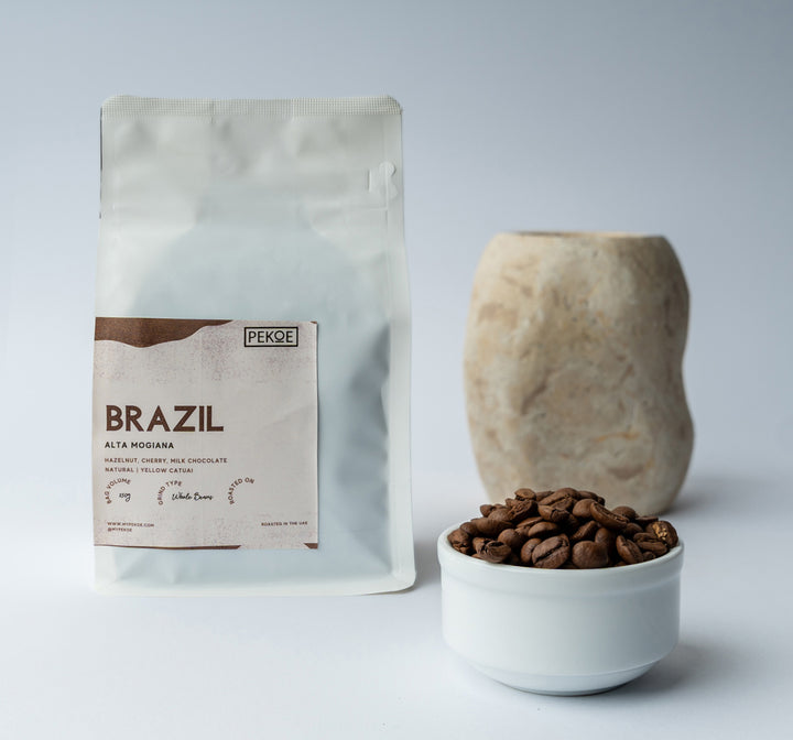 A package of Brazil coffee beans next to a small white bowl filled with coffee beans, against a neutral background.