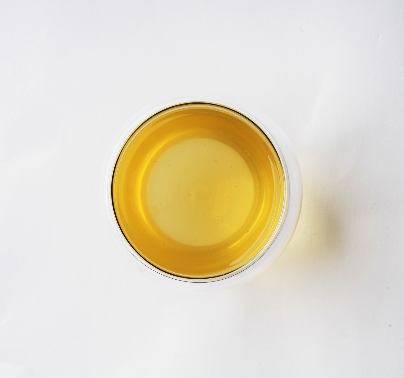 A top-down view of a clear glass tumbler filled with a translucent Darjeeling Green Pearls tea, set against a clean white background.